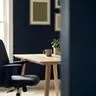 Empty office chair pulled back from a clean wooden desk in a small-business workspace with deep navy walls, muted green accents, and soft natural window light, leaving generous negative space on the right.